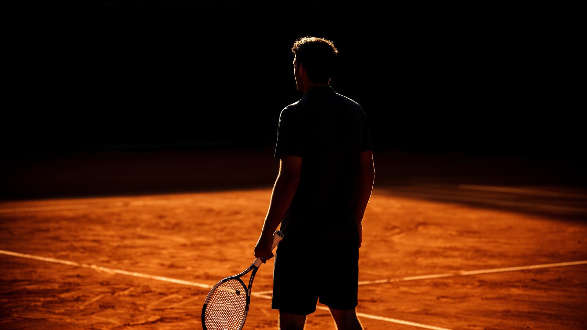 Tennis coach silhouetted on a clay court at golden hour